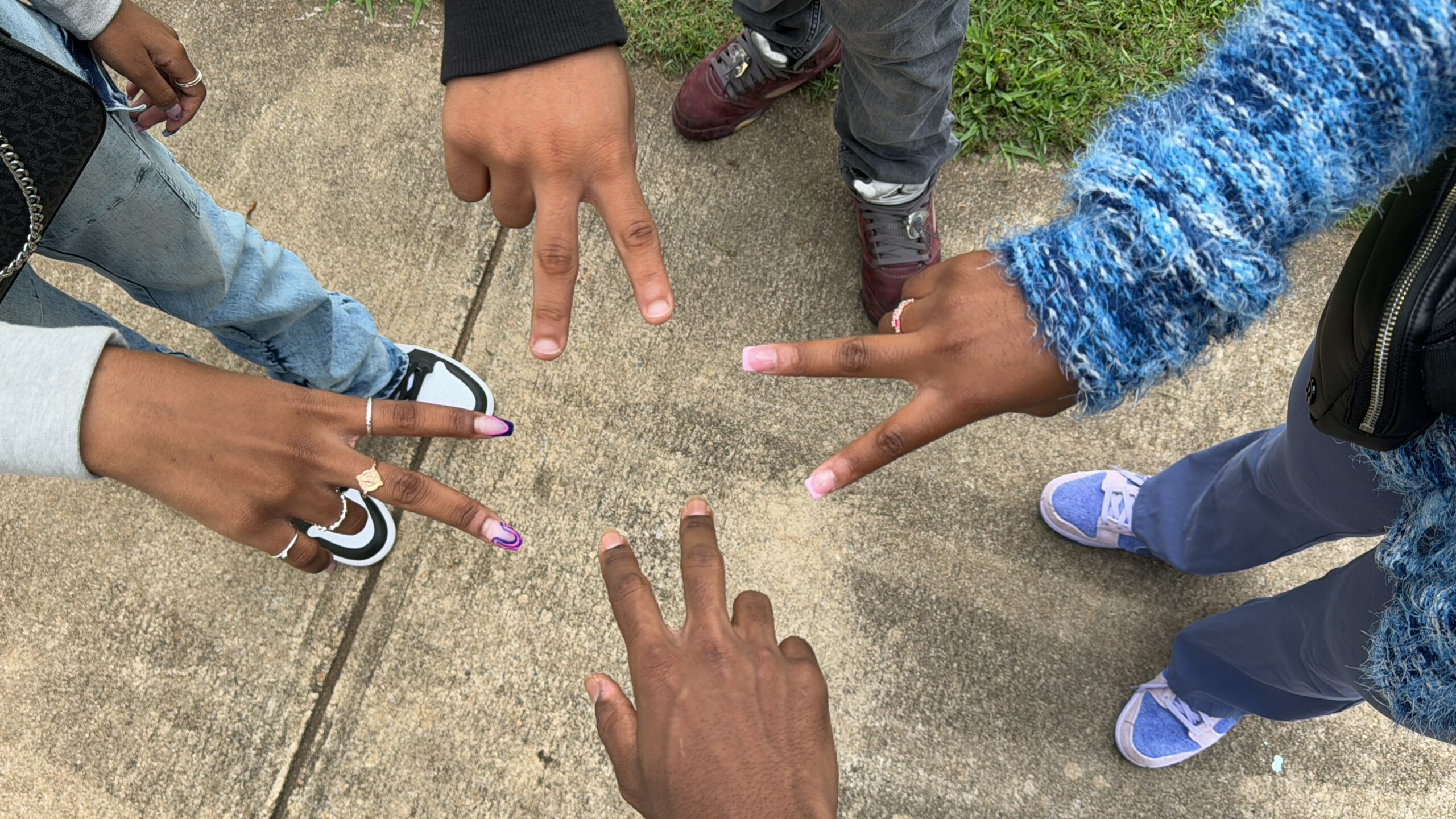 Four students in a circle making peace signs together in mentoring group community